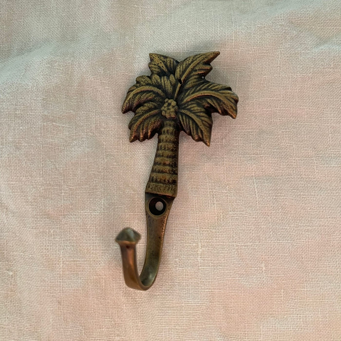 Antique brass coconut palm hook small size showing detailed frond and textured trunk on linen
