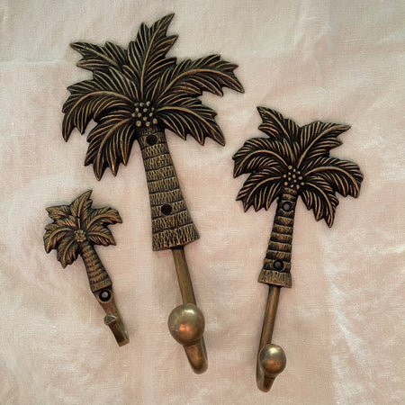 Antique brass coconut palm wall hooks in small medium and large sizes on linen background
