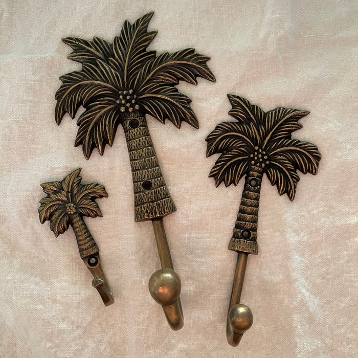 Antique brass coconut palm wall hooks in small medium and large sizes on linen background
