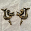 Set of two antique brass mermaid wall hooks facing each other in mirrored display on linen background
