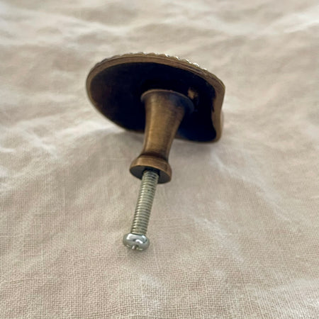 Antique brass scallop shell drawer knob back view showing turned brass stem and screw fitting on linen
