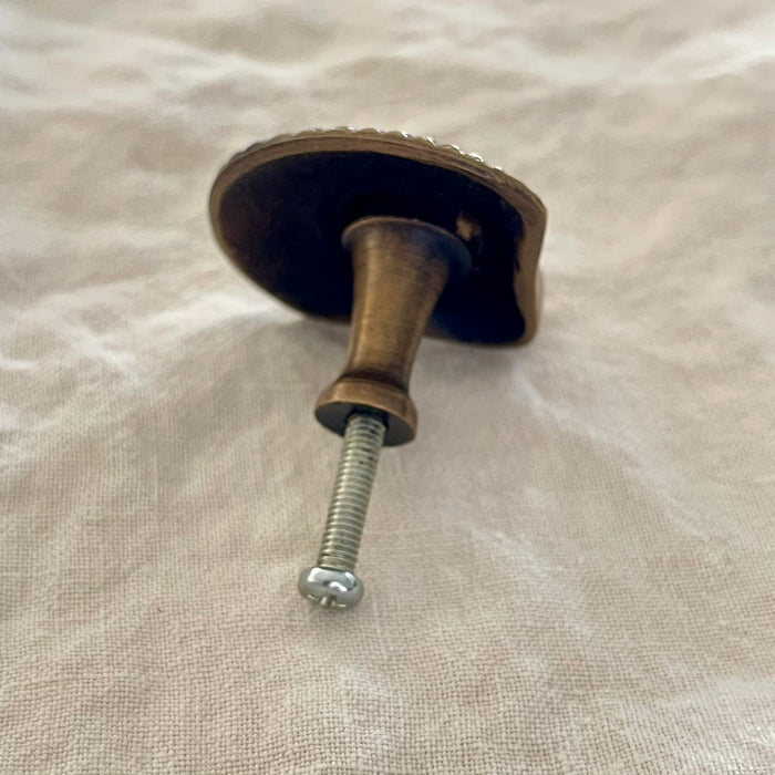 Antique brass scallop shell drawer knob back view showing turned brass stem and screw fitting on linen
