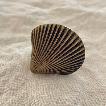 Antique brass scallop shell drawer knob with deep radiating ridges and aged finish on linen background
