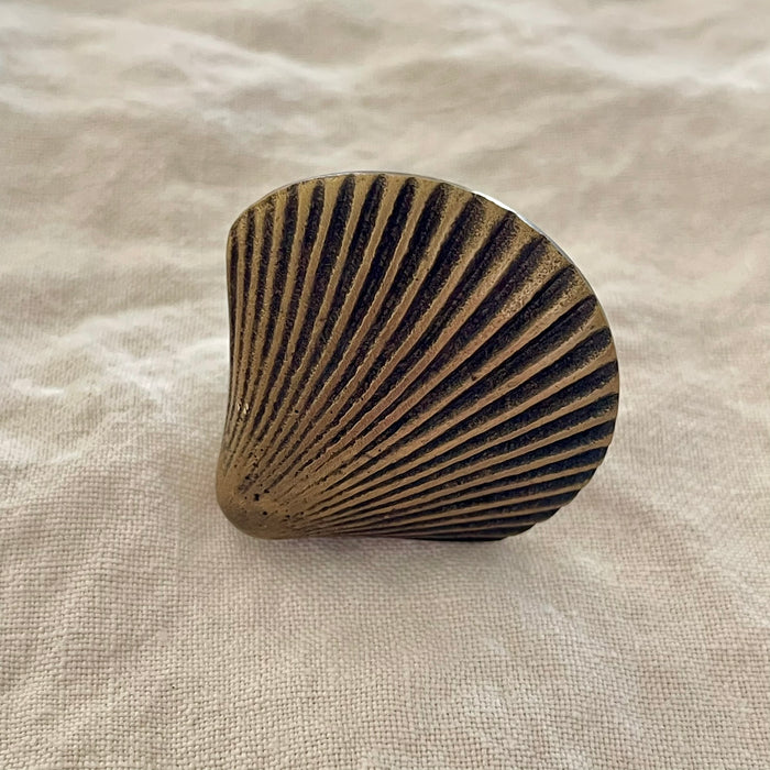Antique brass scallop shell drawer knob with deep radiating ridges and aged finish on linen background
