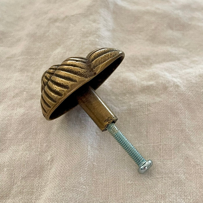 Antique brass spiral shell drawer knob underside view showing brass stem and screw fitting on linen
