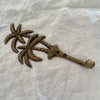 Antique brass twin palm wall hook angled side view showing hook arm depth and palm tree detail on linen
