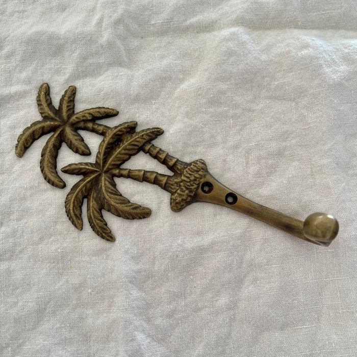 Antique brass twin palm wall hook angled side view showing hook arm depth and palm tree detail on linen
