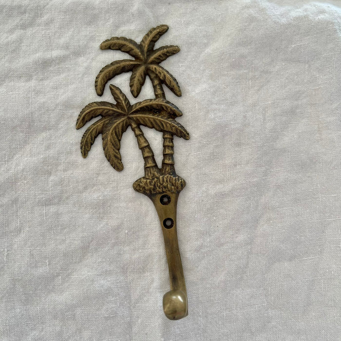 Antique brass twin coconut palm wall hook with detailed textured fronds and segmented trunks on linen background
