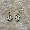 Close-up of handmade cowrie shell earrings with blue and white seed beads
