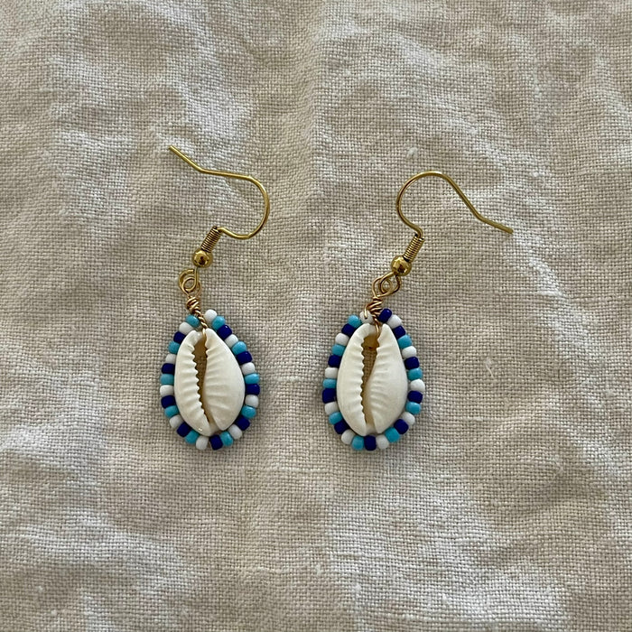 Close-up of handmade cowrie shell earrings with blue and white seed beads
