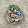 Collection of beaded cowrie shell earrings in multiple colours displayed on a natural shell dish
