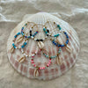 Collection of beaded hoop earrings with cowrie shell drops in multiple colours displayed on a large natural shell
