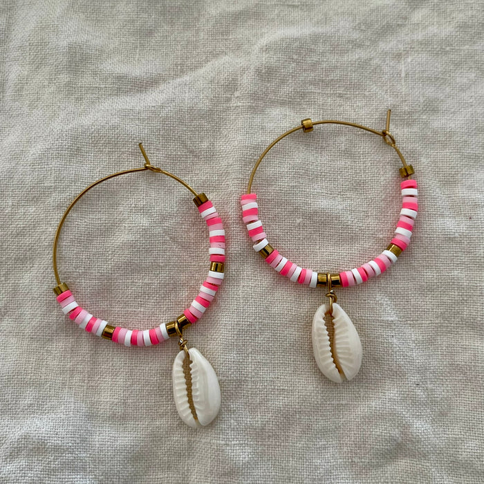 Pink and white polymer clay bead hoop earrings with natural cowrie shell drop on linen background
