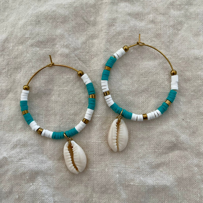 Turquoise and white polymer clay bead hoop earrings with natural cowrie shell drop on linen background
