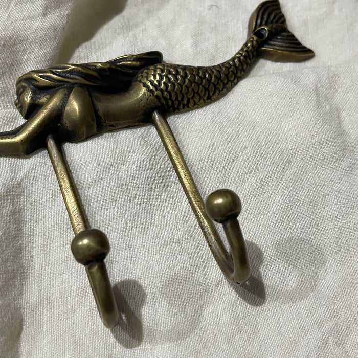 Close-up of two antique brass hooks with rounded ball tips on brass mermaid wall hook
