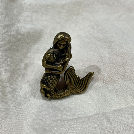 Antique brass mermaid drawer knob with shell detail, front view on white linen background
