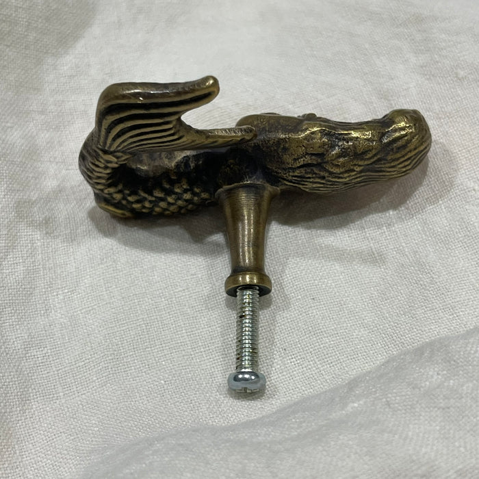 Rear view of brass mermaid drawer knob showing screw bolt and mermaid tail on white linen
