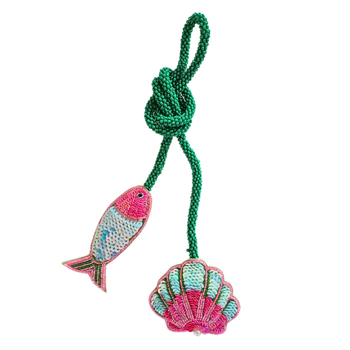 Shell and fish bag charm with pink and aqua bead and sequin detailing, hanging from a green beaded cord loop
