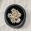 White cowrie shell flower charms in a dark bowl - Travel and Tide Coastal Notions
