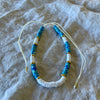 Dark blue polymer clay bead anklet with gold-tone rings and white shell beads on adjustable white cord
