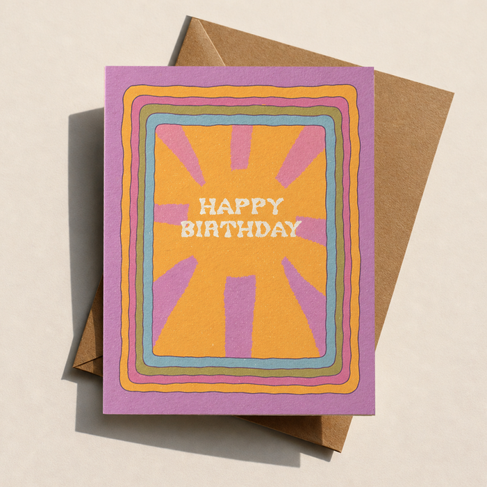 Retro sunburst happy birthday card in amber lilac pink blue and olive with recycled kraft envelope on cream background
