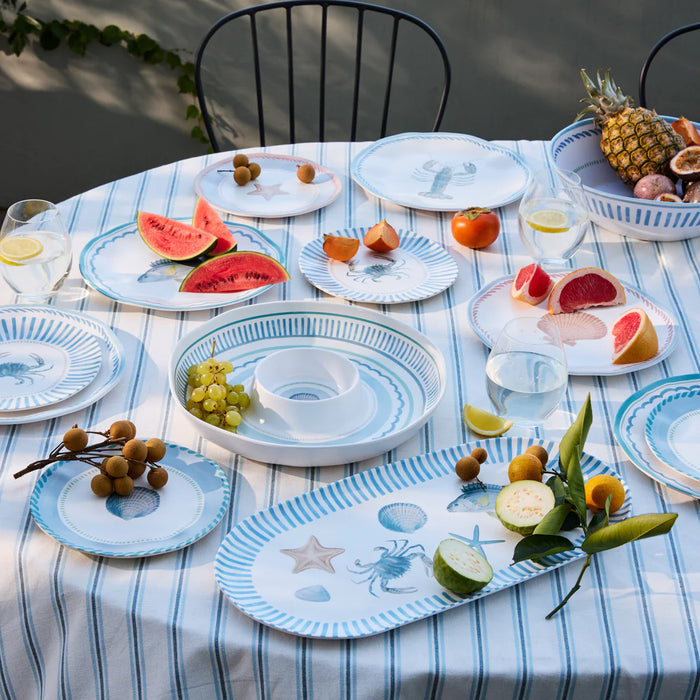Table setting with plates, fruit, and a pineapple on a striped tablecloth.