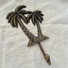 Large antique brass twin palm wall hook angled side view showing hook arm depth and palm tree detail on linen
