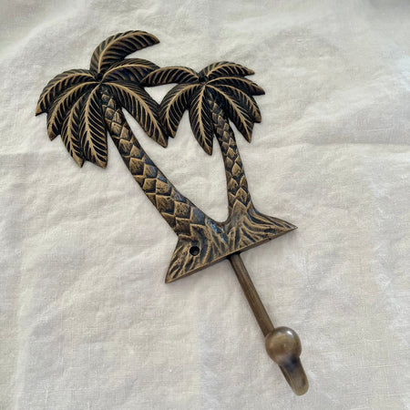 Large antique brass twin palm wall hook angled side view showing hook arm depth and palm tree detail on linen
