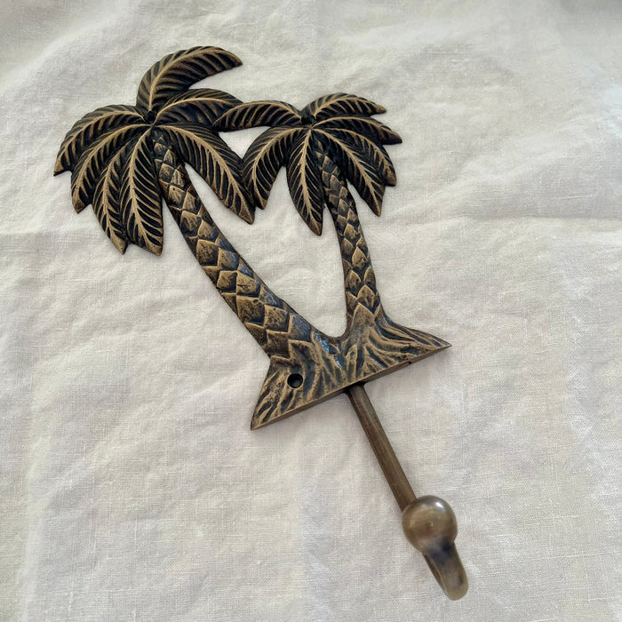 Large antique brass twin palm wall hook angled side view showing hook arm depth and palm tree detail on linen

