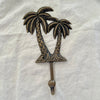 Large antique brass twin coconut palm wall hook with diamond-scale trunks and etched fronds on linen background
