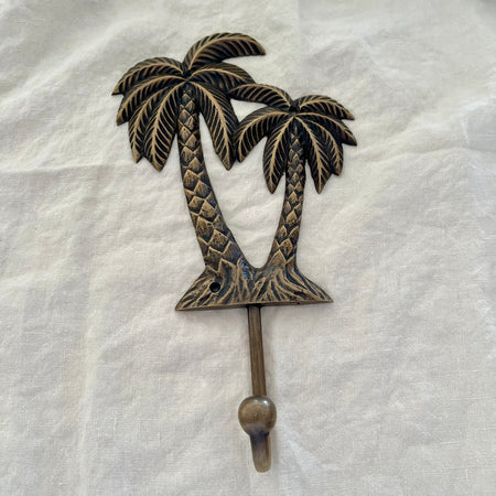 Large antique brass twin coconut palm wall hook with diamond-scale trunks and etched fronds on linen background
