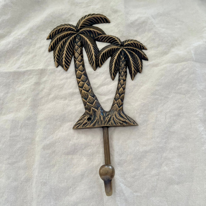 Large antique brass twin coconut palm wall hook with diamond-scale trunks and etched fronds on linen background
