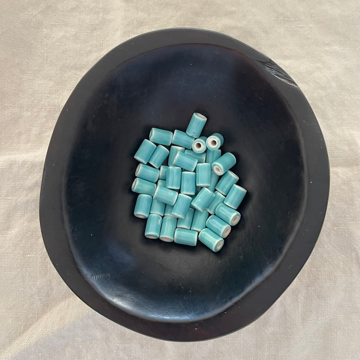 Light teal ceramic barrel beads in a dark bowl - Travel and Tide Coastal Notions
