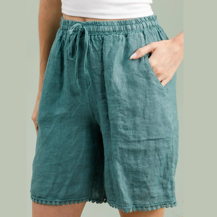 100% linen Bermuda shorts in duck green with pom-pom trim hem and drawstring waist worn by model
