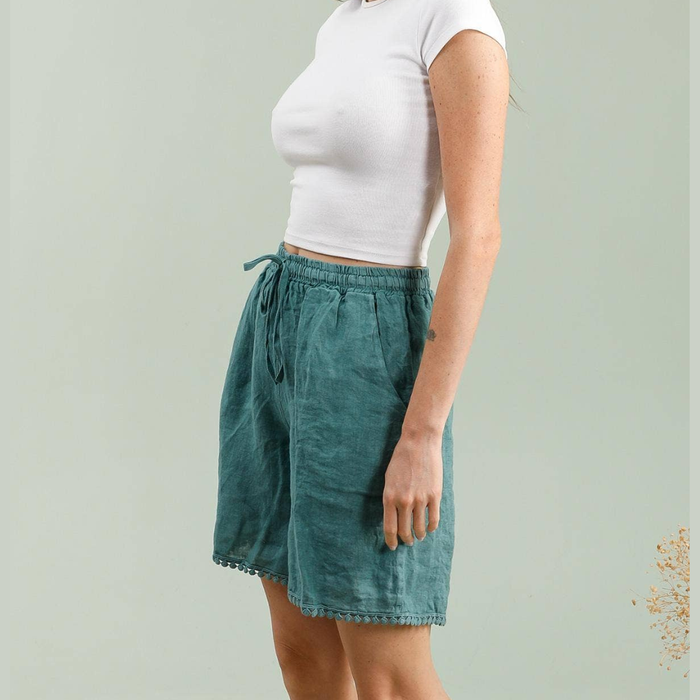 100% linen Bermuda shorts in duck green side view showing relaxed fit drawstring waist and pom-pom trim hem worn by model
