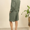 100% linen wide-leg Bermuda shorts in duck green back view worn by model with linen jacket and tropical plant
