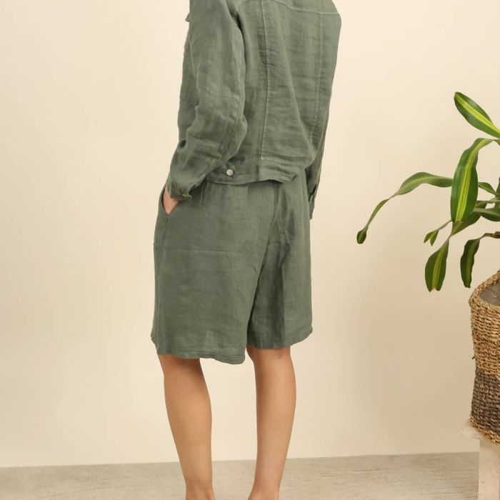 100% linen wide-leg Bermuda shorts in duck green back view worn by model with linen jacket and tropical plant
