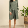 100% linen wide-leg Bermuda shorts in duck green front view worn by model with linen jacket and tropical plant
B