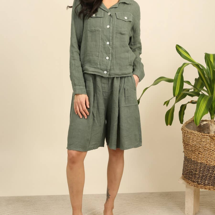 100% linen wide-leg Bermuda shorts in duck green front view worn by model with linen jacket and tropical plant
B