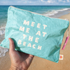 Meet Me at the Beach pouch laid flat showing bold coastal typography and crinkled Tyvek texture
