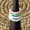 Four pastel shell disc stretch rings stacked on a wooden cone display, showing pink, green, white and blue colourways
