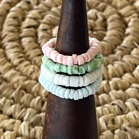 Four pastel shell disc stretch rings stacked on a wooden cone display, showing pink, green, white and blue colourways
