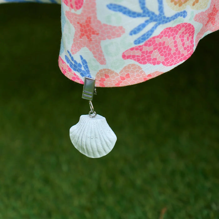 Shell tablecloth weight clips attached to the edge of a tablecloth on an outdoor dining table
