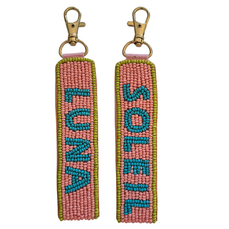 Front and back views of a coral-pink beaded keychain with turquoise SOLEIL and LUNA lettering, olive-green edging and a gold-tone clasp
