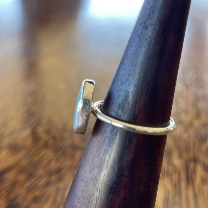 Sterling silver seaglass ring on wooden cone, angled top view showing slim hammered band profile and bezel edge detail
