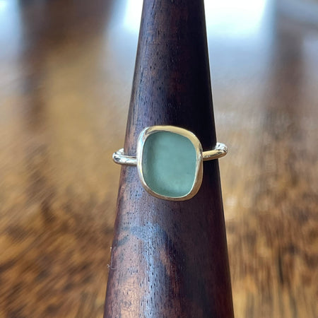 Sterling silver blue seaglass ring on wooden cone, front view showing natural aqua seaglass stone and clean open bezel setting
