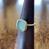 Sterling silver blue seaglass ring on wooden ring cone, side view showing freeform aqua seaglass in simple bezel setting with slim hammered band
