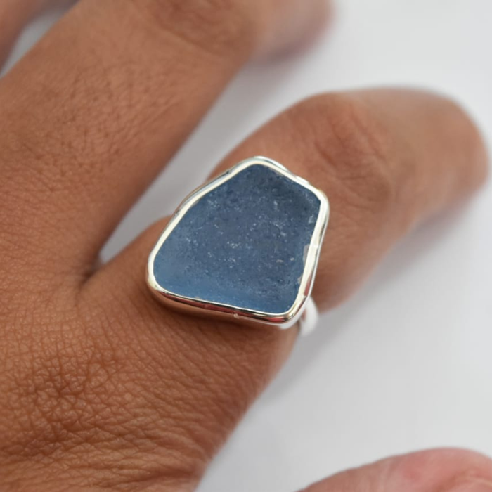 Sterling silver blue seaglass ring worn on hand, showing fit and scale of the freeform deep blue seaglass stone in bezel setting
