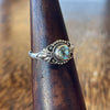 Sterling silver blue topaz ring on wooden cone, top-down angled view showing rope-twist setting, bead surround and decorative scrollwork detail
