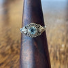 Sterling silver blue topaz detailed ring on wooden ring cone, front view showing round-cut blue topaz in rope-twist bezel with scrollwork and bead surround
